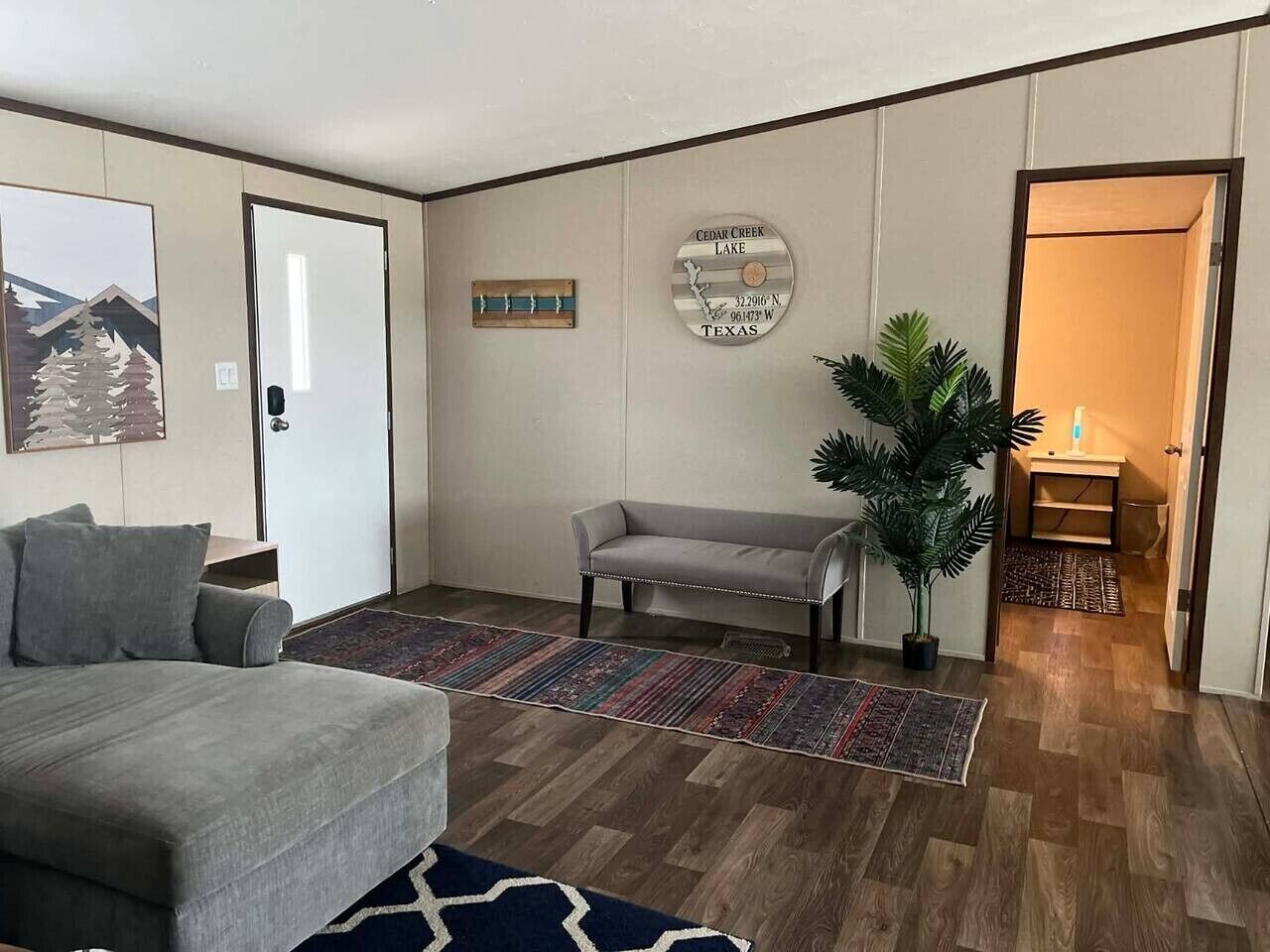 A living room with a sofa, a bench, a potted plant, a rug, and a wall clock.