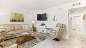 A living room with a beige sofa, a glass coffee table, a beige armchair, and a flat-screen TV mounted on the wall. - Beach Life, ground floor, quiet &clean. 2BR 2 Bath (Saint Augustine)