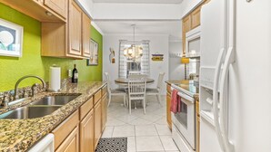 A compact kitchen with wooden cabinets, a granite countertop, a sink, a dining table with chairs, and a refrigerator. - Beach Life, ground floor, quiet &clean. 2BR 2 Bath (Saint Augustine)