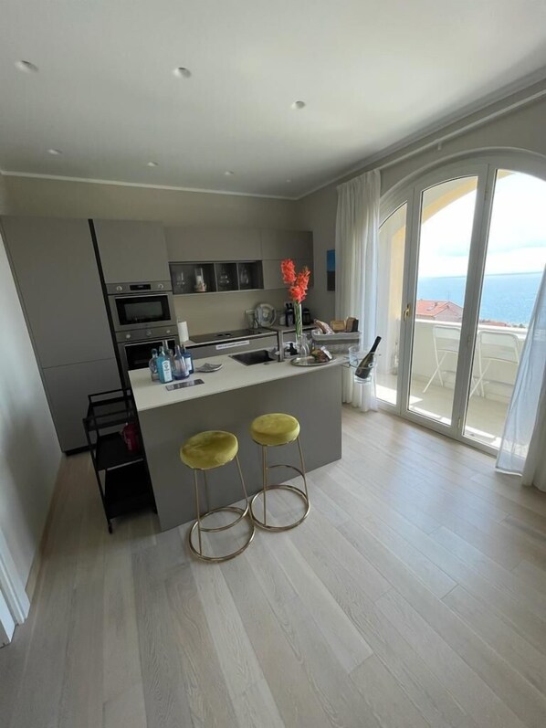 Cocina moderna con isla central, taburetes de bar y vistas al mar a través de amplios ventanales correderas.