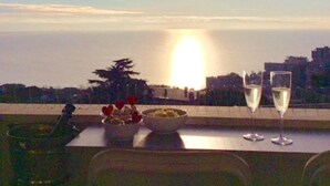 Un balcon avec une table dressée pour deux personnes, un panier de fruits et deux coupes de champagne.