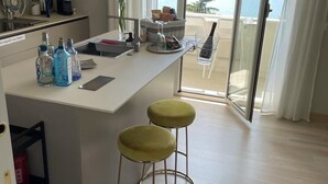 Une cuisine moderne dotée d’un îlot central, de tabourets de bar et offrant une vue sur la mer grâce à une porte vitrée.
