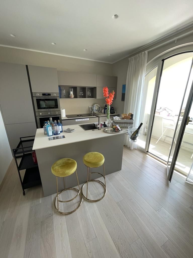 Une cuisine moderne dotée d’un îlot central, de deux tabourets de bar et offrant une vue sur l’espace extérieur grâce à une porte vitrée.