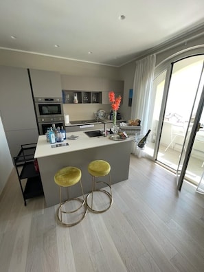 Een moderne keuken met een centraal eiland, twee barkrukken en uitzicht op het buitengebied door een glazen deur.