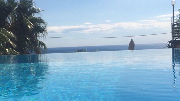 Une piscine d’eau cristalline, d’un bleu éclatant, avec vue sur l’océan et les palmiers.
