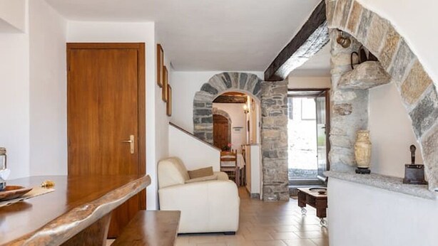 A modern interior with a wooden bar, a white sofa, stone archway, and a stone fireplace. - Art Nature and Tranquility (casalzuigno)