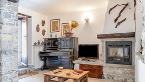 A rustic living room with a stone fireplace, a television, and a wooden coffee table. - Art Nature and Tranquility (casalzuigno)