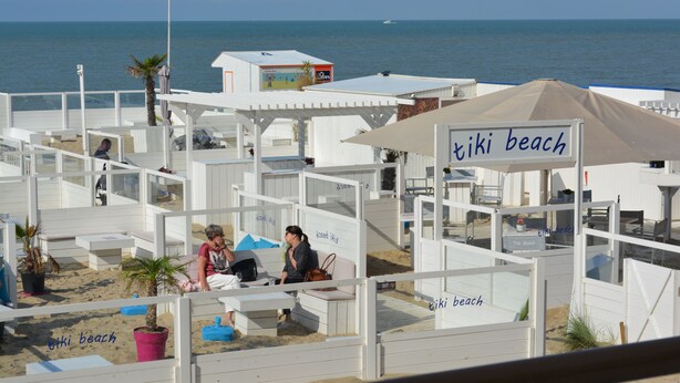 Un hôtel en bord de mer avec des cabanes blanches, un parasol et une vue sur la mer.