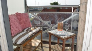 Un balcon avec un banc en bois, une table avec un verre et une couverture rose.