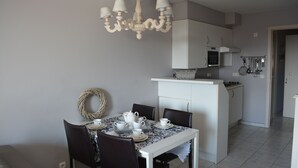 Un coin repas avec une table dressée pour quatre personnes, un lustre et une cuisine en arrière-plan.