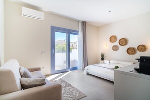 A modern bedroom with a bed, a sofa, a coffee machine, and a view through a sliding door.