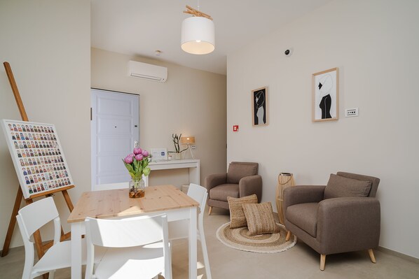 A modern living room with a wooden table, white chairs, a brown sofa, and a painting on the wall.