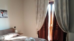 Une chambre à coucher avec un lit, un plancher en bois, des rideaux et une lampe fixée au mur.
