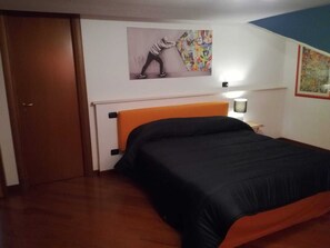 Een slaapkamer met een bed, een deur, een nachtkastje en een muur met twee kunstwerken.