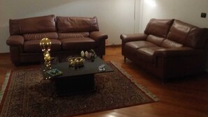 Un salon avec deux canapés en cuir marron, une table basse foncée et un tapis à motifs.