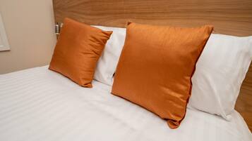 A bed with white bedding and two orange pillows.
