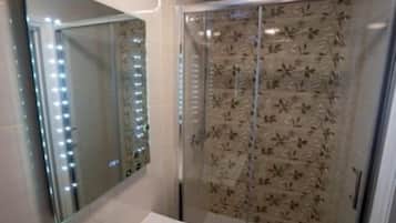 Een badkamer met een grote spiegel, een wastafel en een douche met deurruitjes met bloemenmotief.