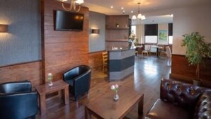 A modern hotel lobby with leather seating, a reception desk, and a TV mounted on the wall. - Eagle Hotel (Luton)