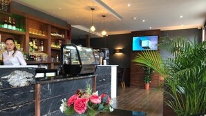A hotel reception area with a marble counter, a coffee machine, a TV screen, and a potted plant. - Eagle Hotel (Luton)