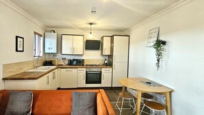 Cocina compacta con comedor, que incluye horno empotrado, cafetera y una pequeña mesa con taburetes.