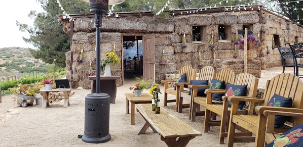 A rustic outdoor seating area with wooden furniture and a thatched-roof building in the background.