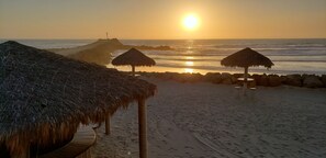 A beach with thatched umbrellas and a rocky breakwater.
