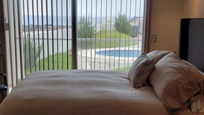 Une chambre dotée d’un grand lit, d’un ventilateur de plafond et offrant une vue sur une piscine et un espace verdoyant.
