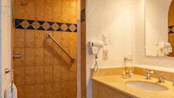 Een badkamer met een beige wastafel, een spiegel en een douchegedeelte met een handgreep.