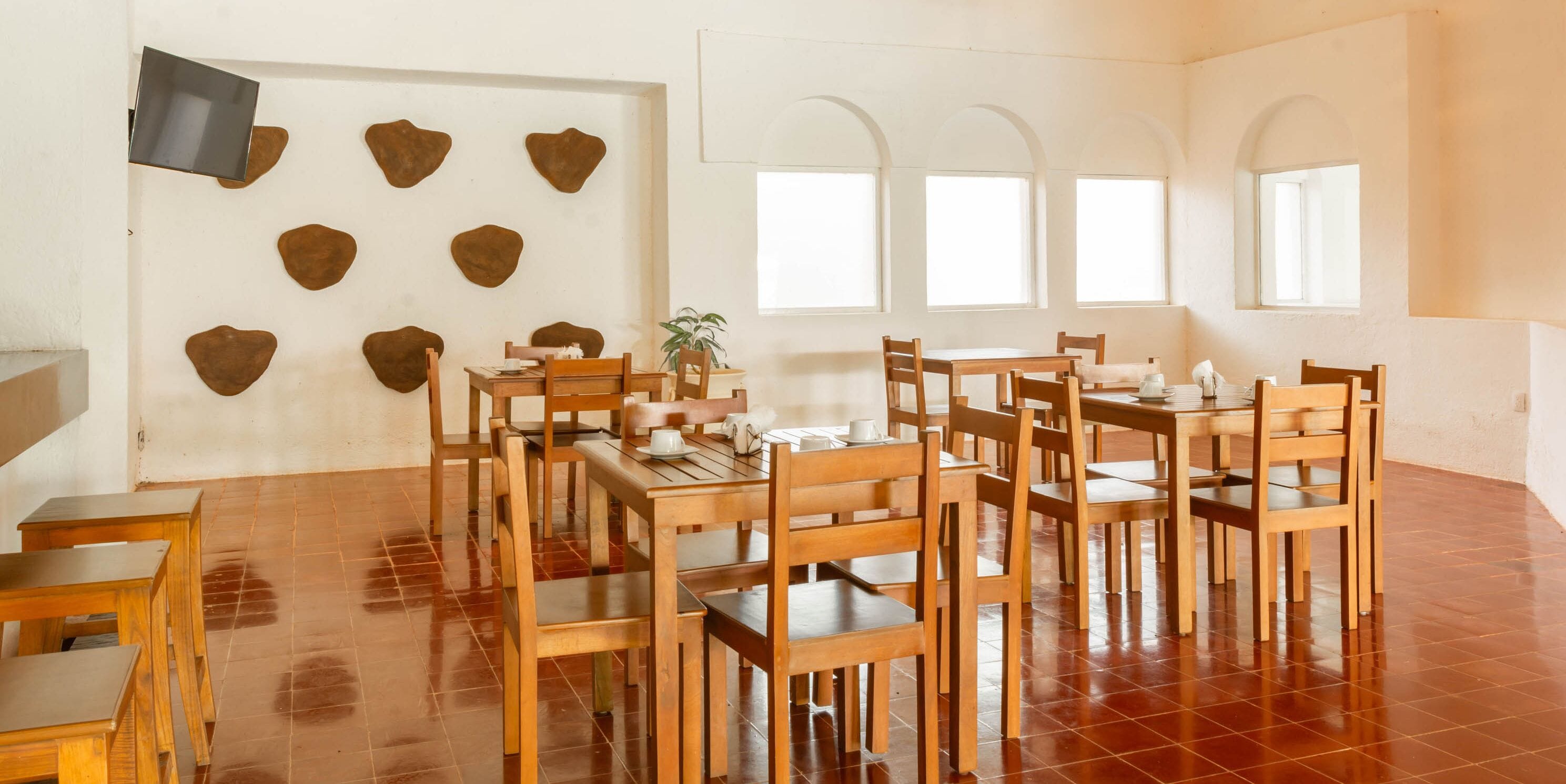 A dining area with wooden tables and chairs, a flat-screen TV mounted on the wall, and a potted plant.