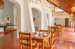 A spacious dining area with wooden tables and chairs, white walls, and a tiled floor.