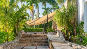 A set of stone steps leading up to a covered area with a beige canopy, surrounded by lush greenery and palm trees. - Kaab Coba (Coba)