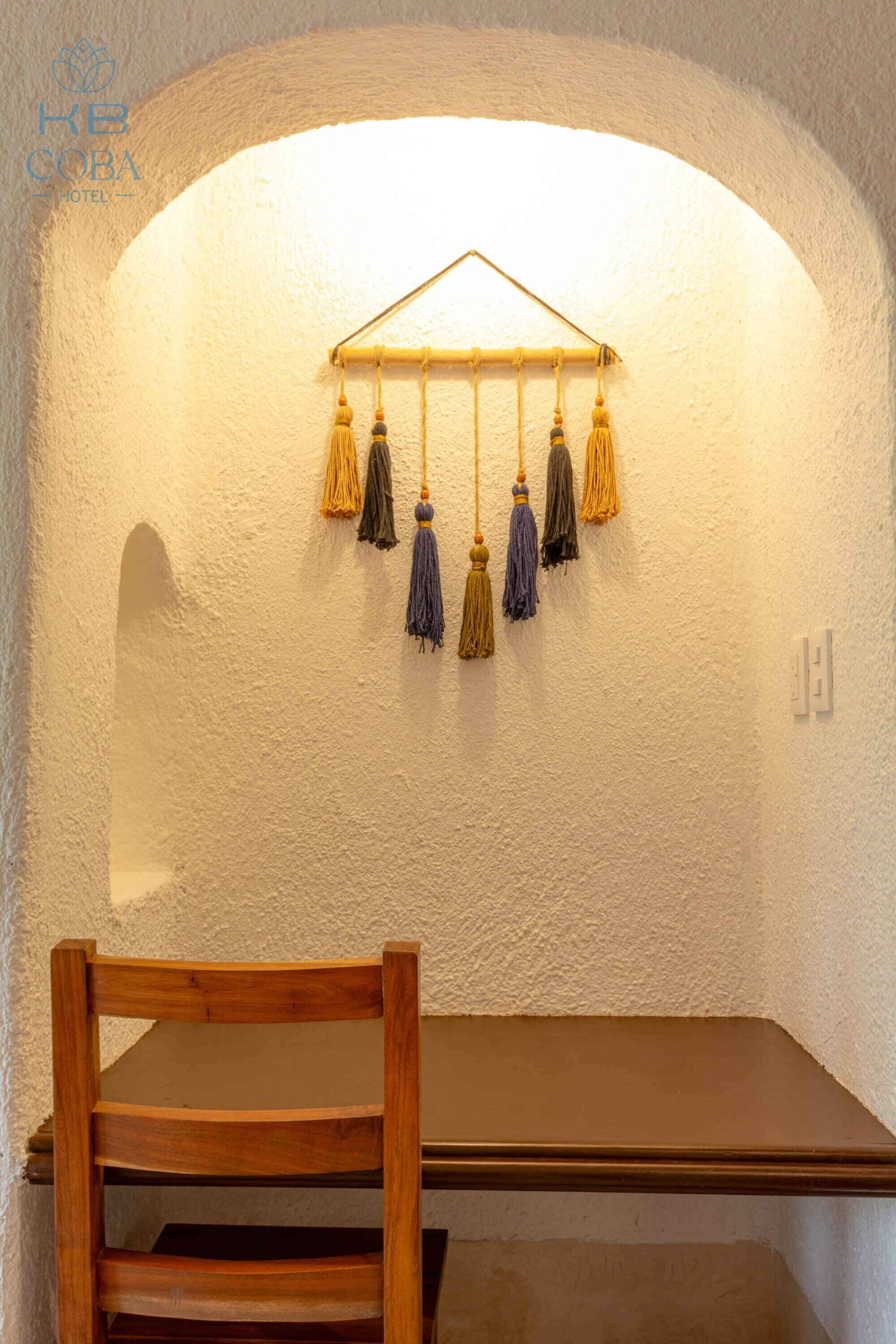 A room with a white textured wall, a wooden table, and a hanging tassel decoration.