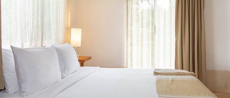 A hotel room with a bed, a nightstand with a lamp, and sheer curtains.