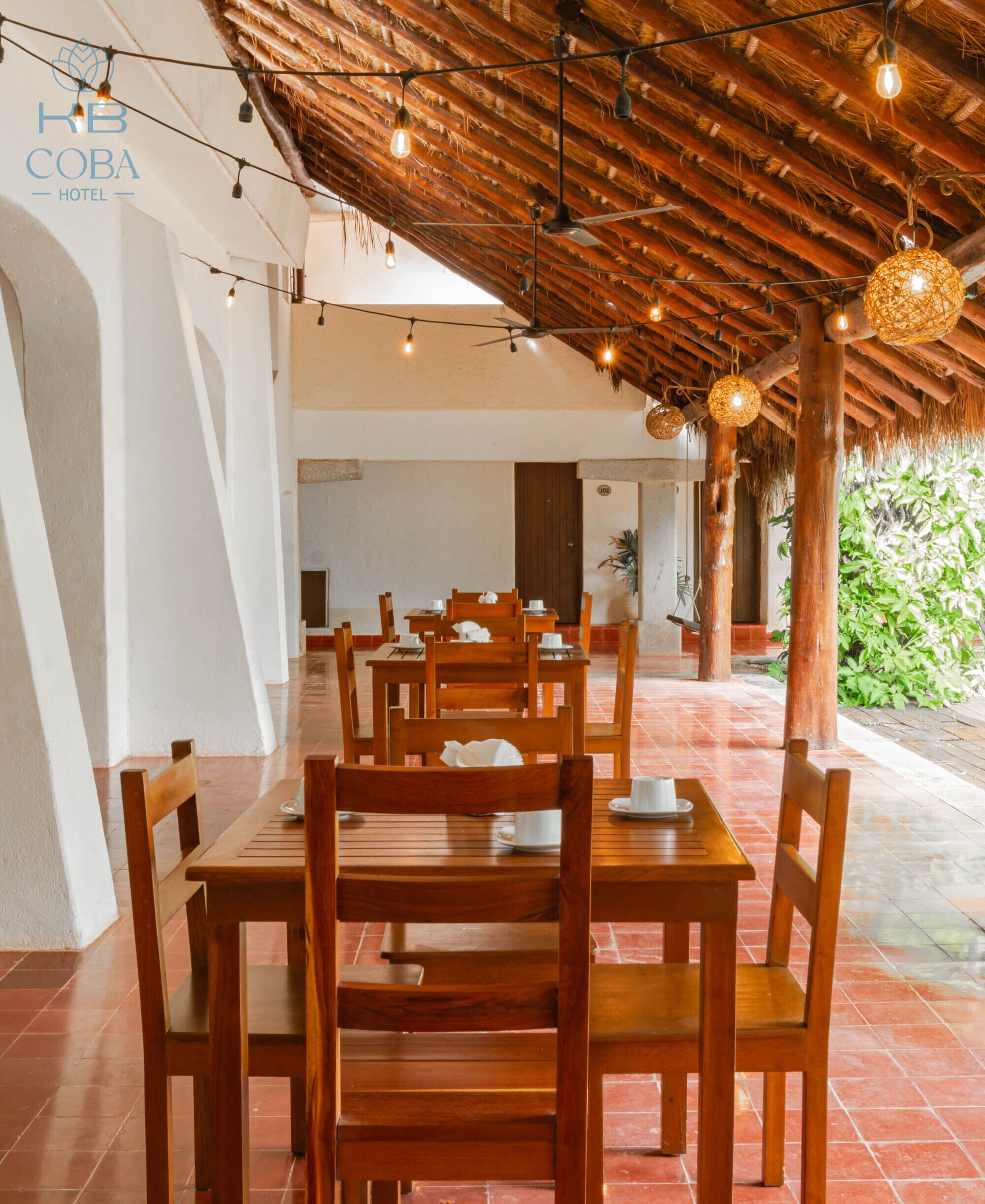 A restaurant with wooden tables and chairs, a thatched roof, and string lights.