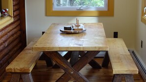 Una mesa de madera con bancos en una habitación con ventana y pared de troncos.