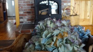 Una habitación rústica con pared de ladrillo, puerta de madera, chimenea y un banco de madera con hortensias.