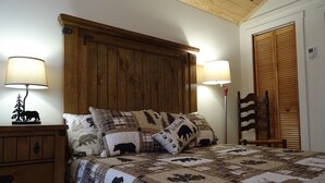 Un dormitorio con cabecera de madera, dos lámparas de noche, una cama con colcha de estampados de animales, una mesita de noche y un armario de madera.