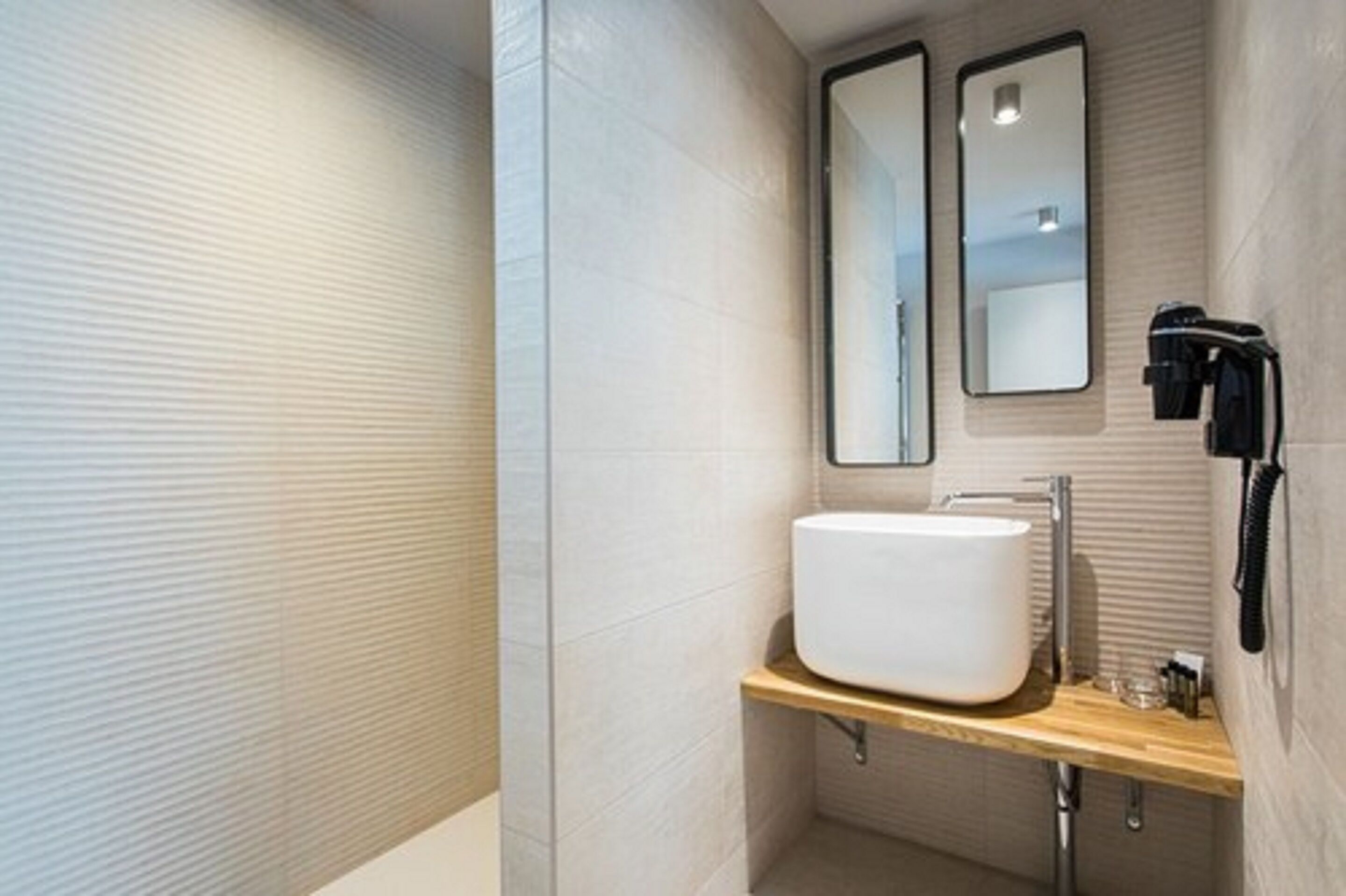 Een moderne badkamer met een groot wit wastafel, twee spiegels en een handdoekrek.