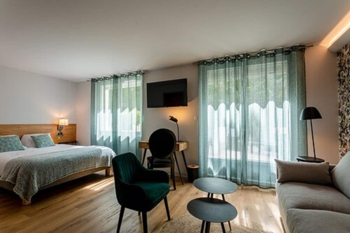 Una habitación de hotel con cama, escritorio, silla, sofá y televisor fijado a la pared.