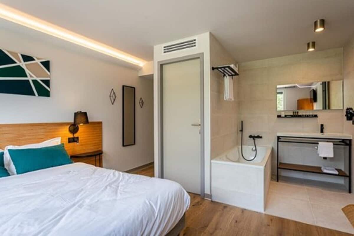 Una habitación de hotel moderna con cama, ducha, lavabo y espejo.