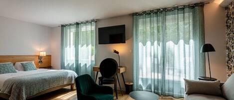 Habitación de hotel con cama, escritorio, silla, sofá y televisor montado en la pared.