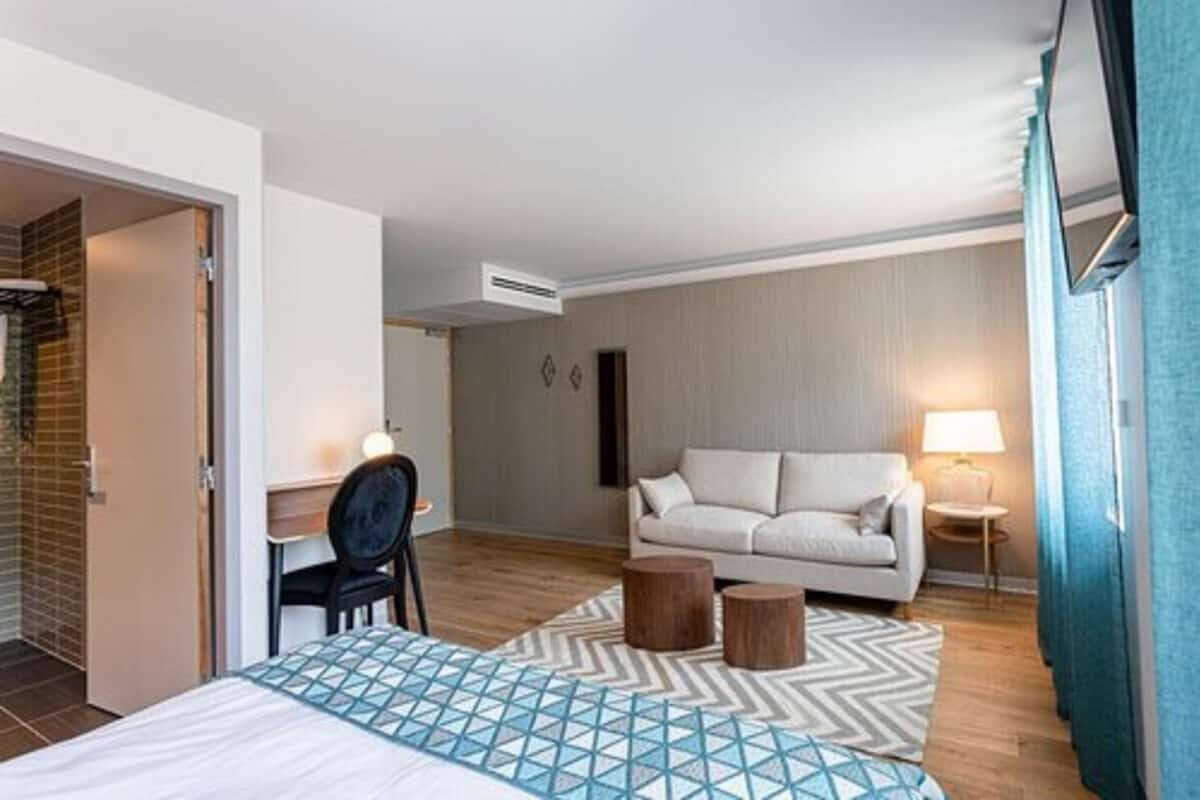 Una habitación de hotel con cama, escritorio, sofá, lámpara y ventana.