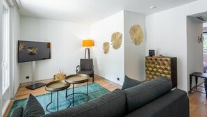 Ein modernes Wohnzimmer mit einer Couch, zwei Beistelltischen, einem Flachbildfernseher, Wanddekoration und einem Möbelkorpus mit Muster.