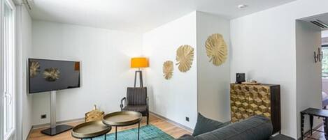 A modern living room with a sofa, two side tables, a flat-screen TV, decorative wall art, and a patterned cabinet.