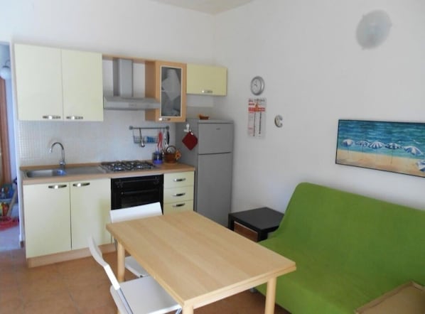 A compact kitchen with a sink, stove, and refrigerator, a small dining table, and a green couch.
