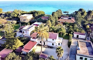 An aerial view of a coastal residential area with houses, palm trees, and a clear view of the sea.