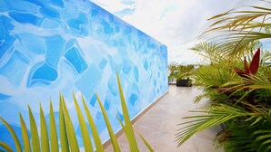 A modern building with a blue mosaic wall, a tiled floor, and tropical plants.