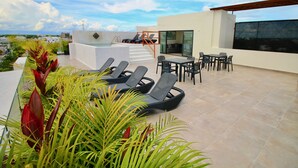 A rooftop terrace with lounge chairs, a table, and a pool area.