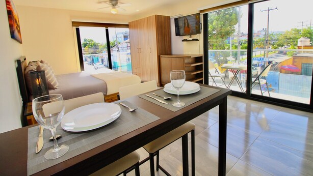 A modern hotel room with a dining area, a bed, and a balcony with a view of the city.