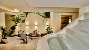A spacious indoor area with a round table and chairs, surrounded by potted plants and a built-in hot tub.